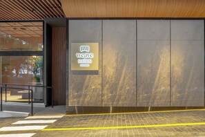 Entrada de un hotel con un cartel que dice 'weave suites', diseño moderno, techo de madera y piso de baldosas.