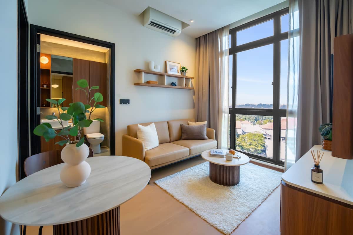A modern living room with a sofa, coffee table, and a dining table with a vase. There is a large window with a view of the city.