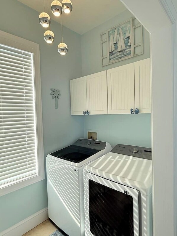 A laundry room with two stacked washer and dryer units, a window with blinds, and a wall-mounted light fixture.