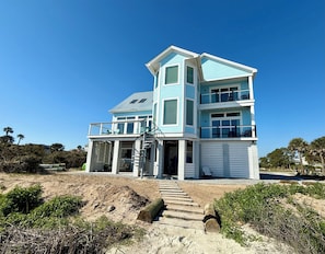 A multi-story beachfront house with a balcony, a staircase leading to the entrance, and a sandy foreground. - Blue Horizon - Oceanfront House on Harbor Island (Harbor Island)