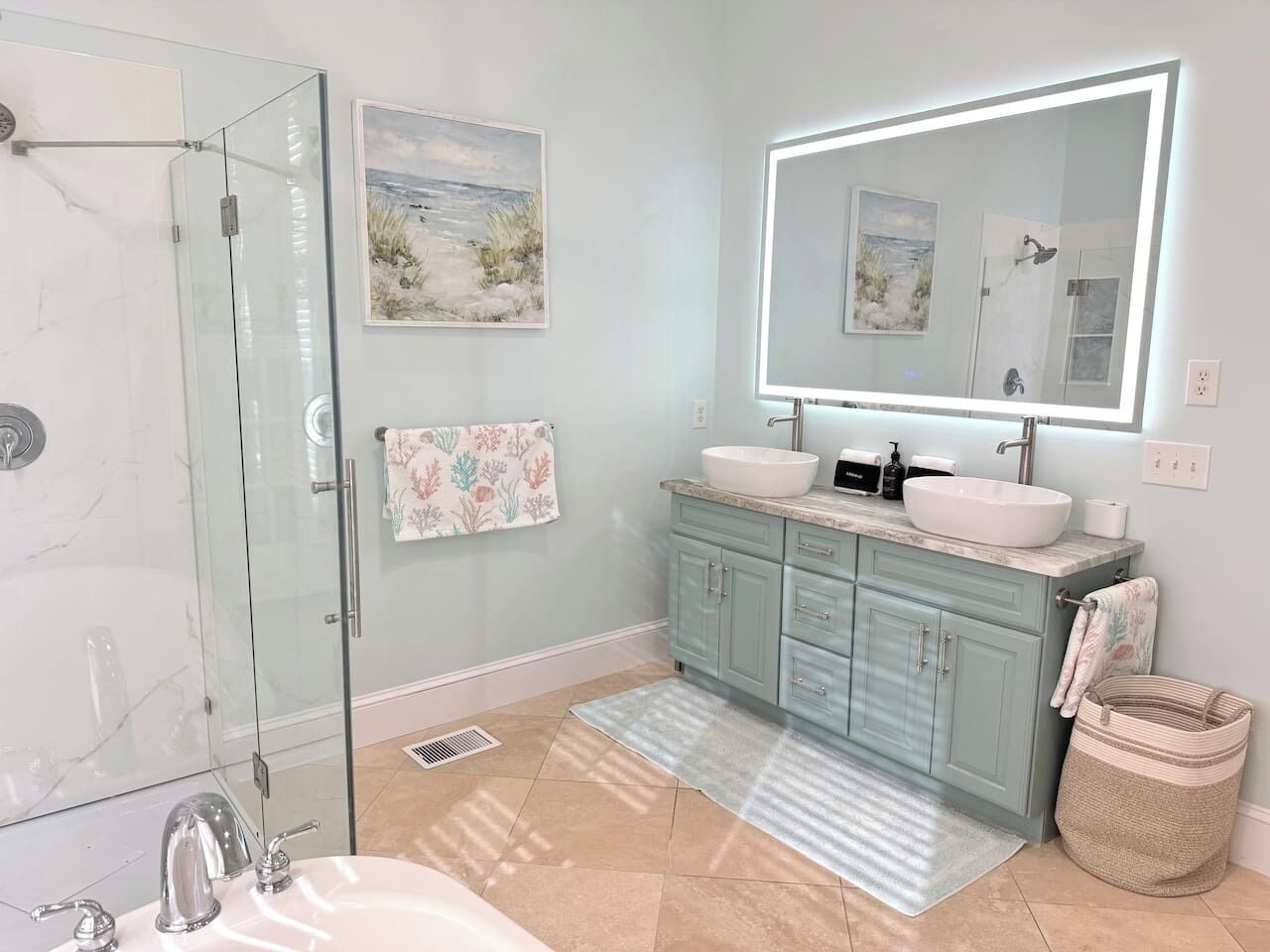 Un bagno con box doccia in vetro, due lavandini, uno specchio grande e un tappeto decorativo.