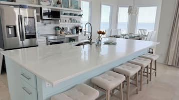 Een moderne keuken met een groot eiland, barstoelen en een eetgedeelte met een kroonluchter.