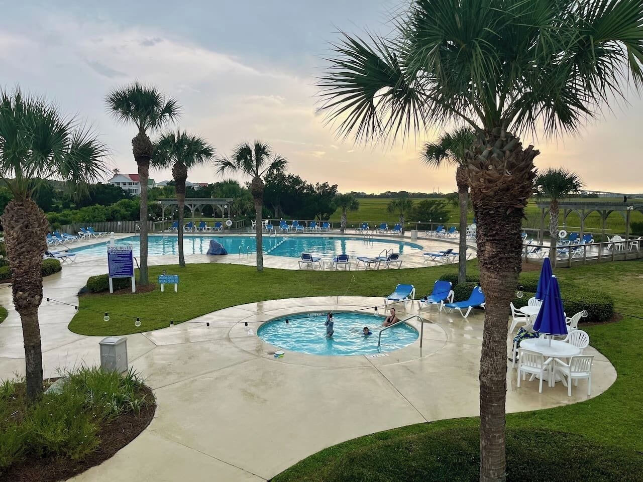 Un área de piscina con varias piscinas, sillas de descanso y palmeras.