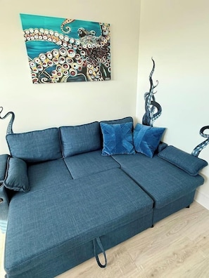 A blue sofa with a matching ottoman, a wall-mounted painting, and a decorative metal piece. - Blue Horizon - Oceanfront House on Harbor Island (Harbor Island)