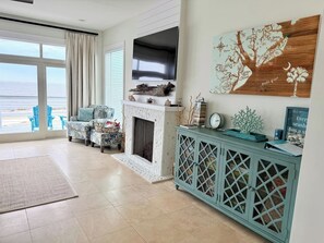 A living room with a fireplace, a television mounted above it, and a view of the ocean through large windows. - Blue Horizon - Oceanfront House on Harbor Island (Harbor Island)
