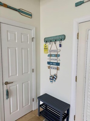 A hallway with a white door, a wall-mounted sign with a beach theme, and a small bench. - Blue Horizon - Oceanfront House on Harbor Island (Harbor Island)