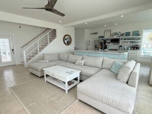 Un salon spacieux avec un grand canapé d’angle, une table basse blanche et un escalier menant à un autre niveau.