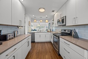 A modern kitchen with white cabinets, stainless steel appliances, and wooden flooring. - New Beach House Rental. Welcome to your Isle of Palms Oasis! (Isle Of Palms)