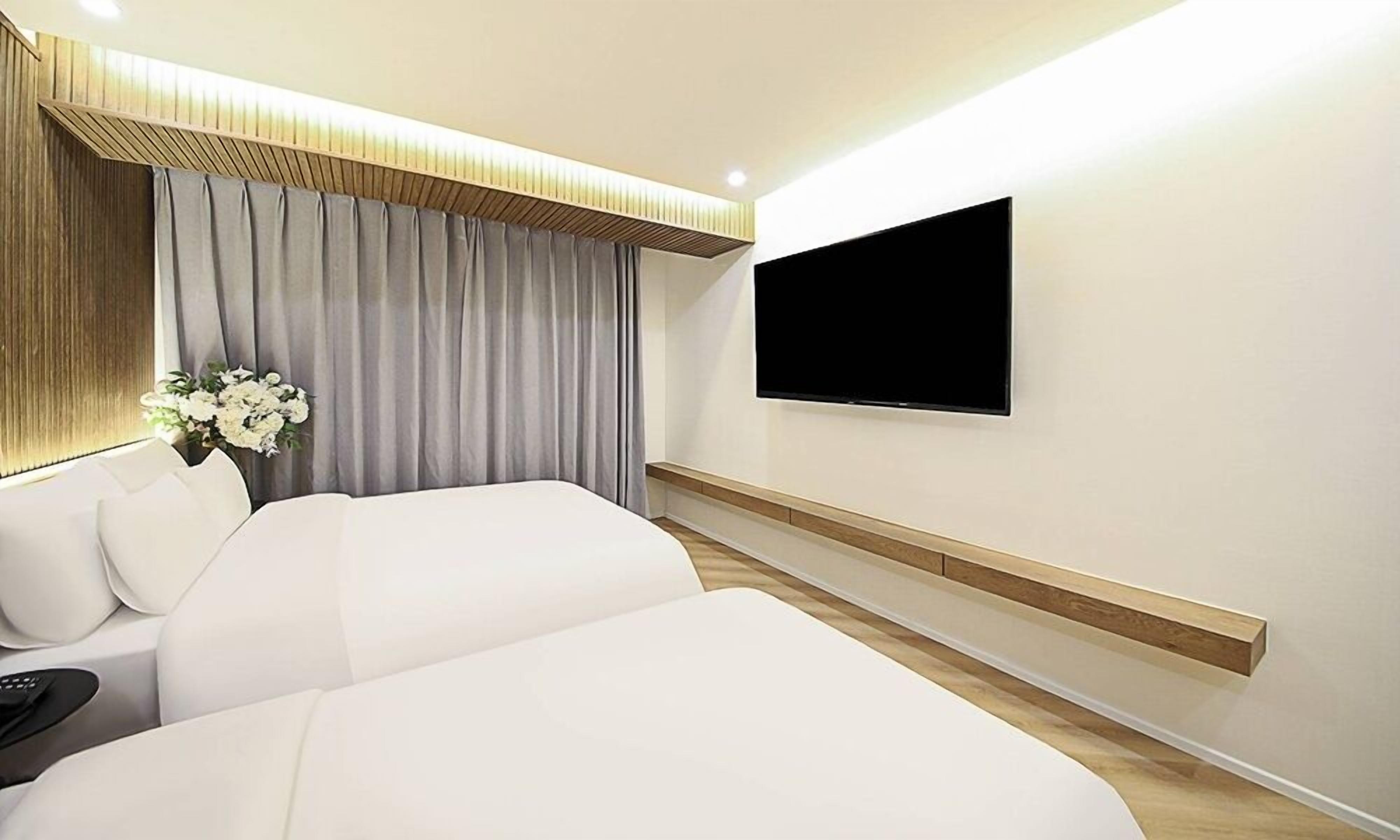 A hotel room with a large bed, a TV mounted on the wall, and a wooden panel design on the ceiling.