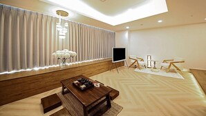 A modern living room with a wooden coffee table, a flat-screen TV, and a seating area with chairs and a small table.