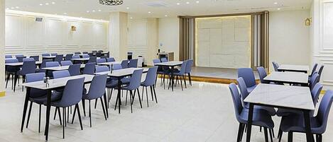 A conference room with multiple tables and chairs, white walls, and a large window with curtains.
