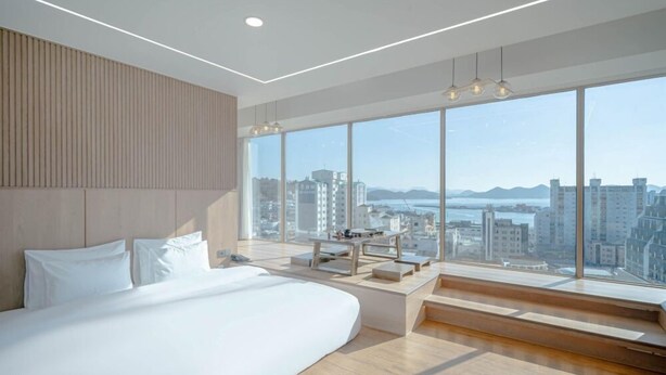 A modern bedroom with a large bed, a desk, and a view of the city.