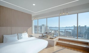 A modern bedroom with a large bed, a desk, and a view of the city. - Tongyeong Tourist Hotel (Tongyeong)