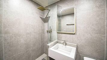 Een moderne badkamer met een douchecabine van glas, een witte wastafel en een spiegel.