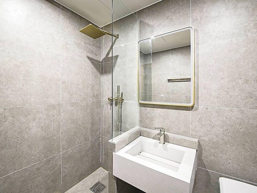 Een moderne badkamer met een douchecabine van glas, een witte wastafel en een spiegel.