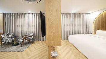 A modern hotel room with a wooden floor, a bed, a desk with a chair, and a large window with curtains.