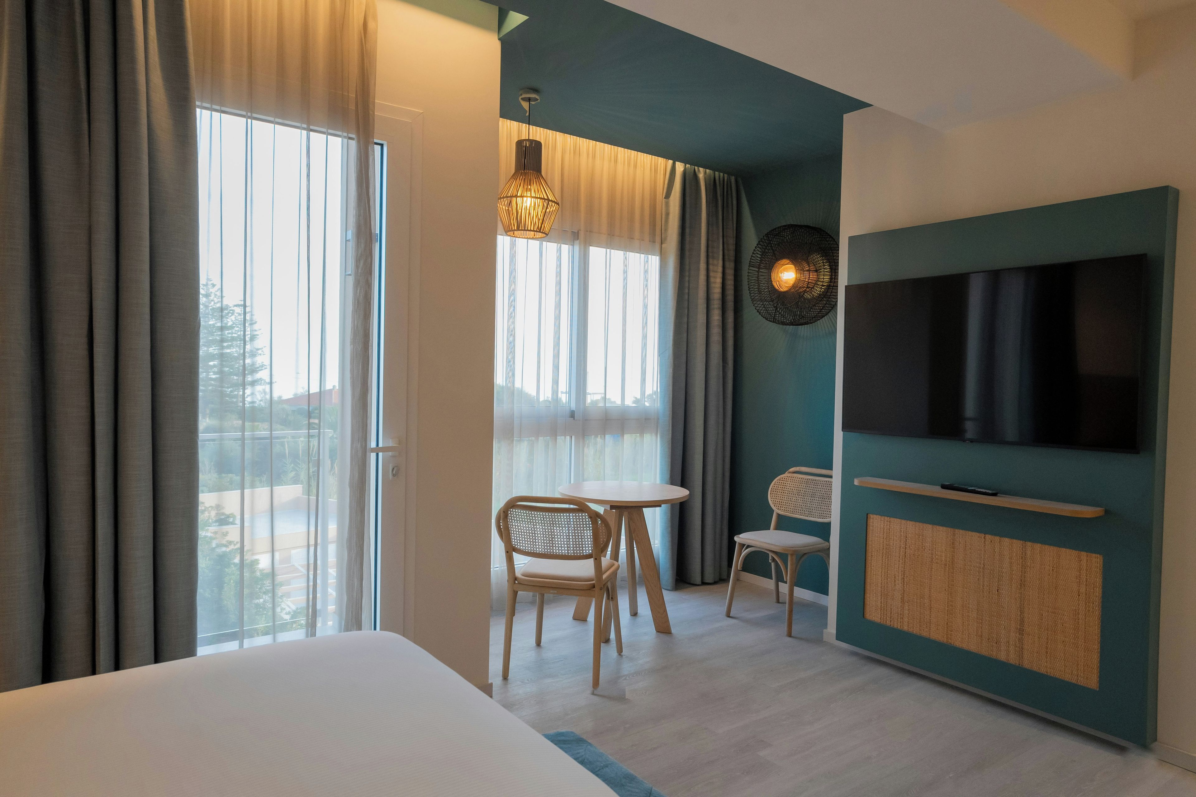 Habitación de hotel con cama, televisor, una pequeña mesa con sillas y vistas al exterior.