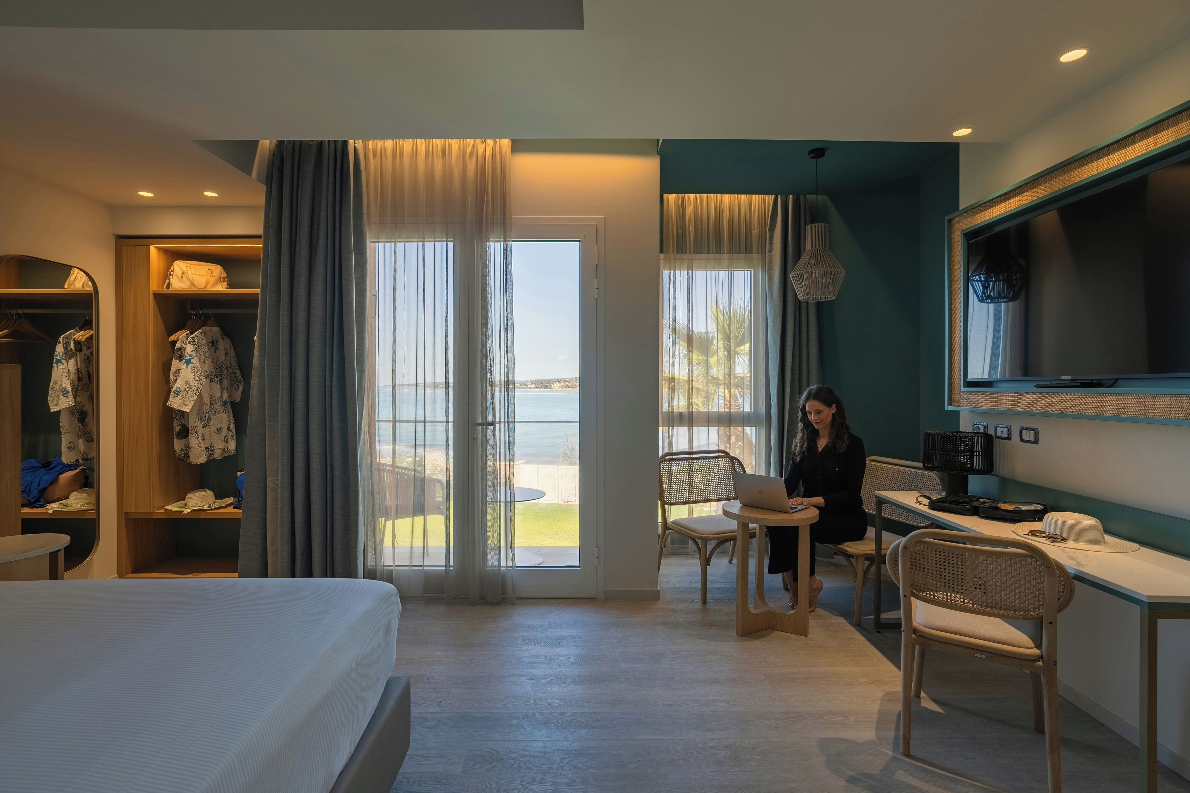 Habitación de hotel con cama, escritorio, laptop, televisor y vista al exterior.