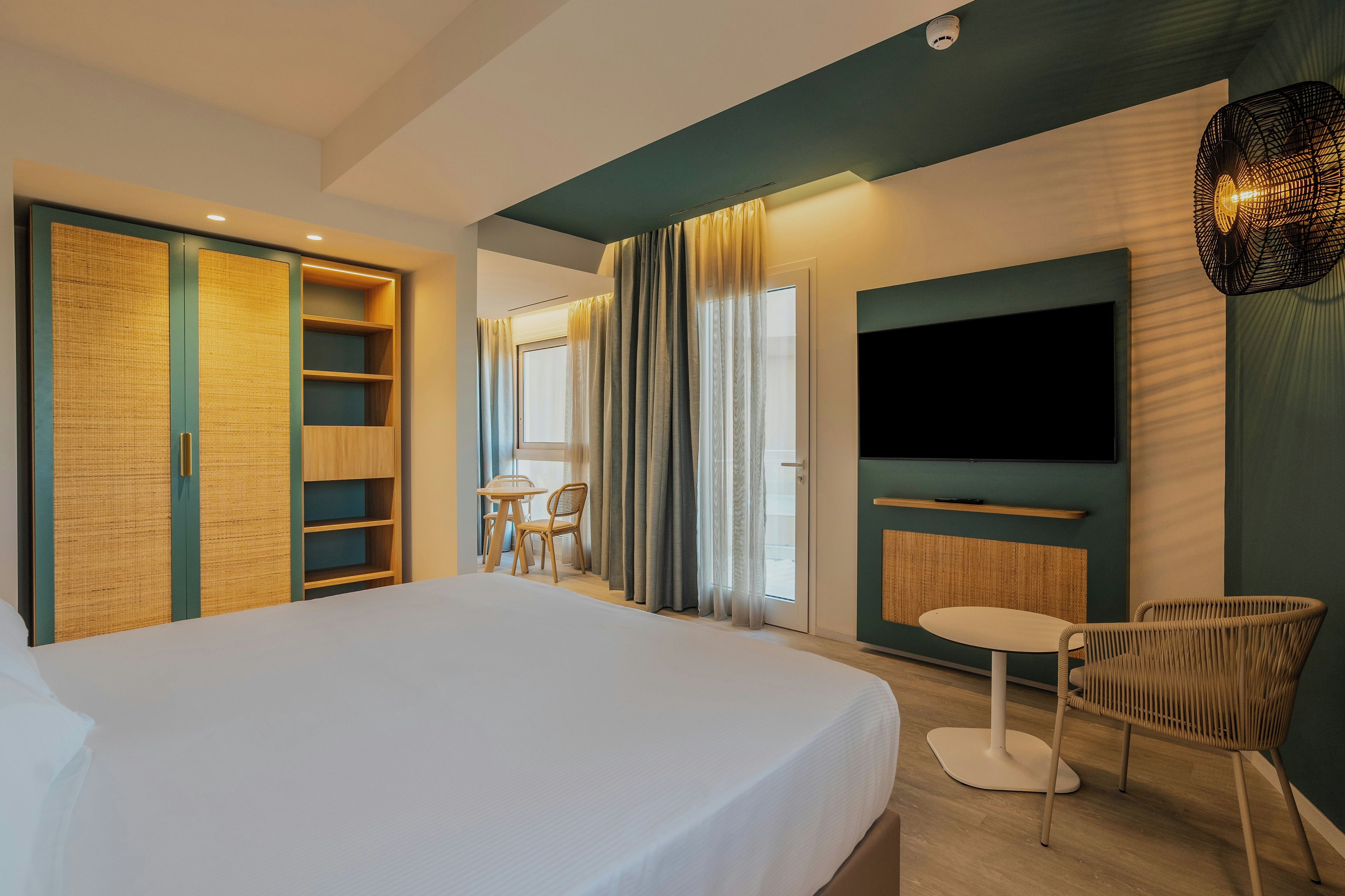 A hotel room with a bed, a TV, a seating area with a chair, and a wardrobe.