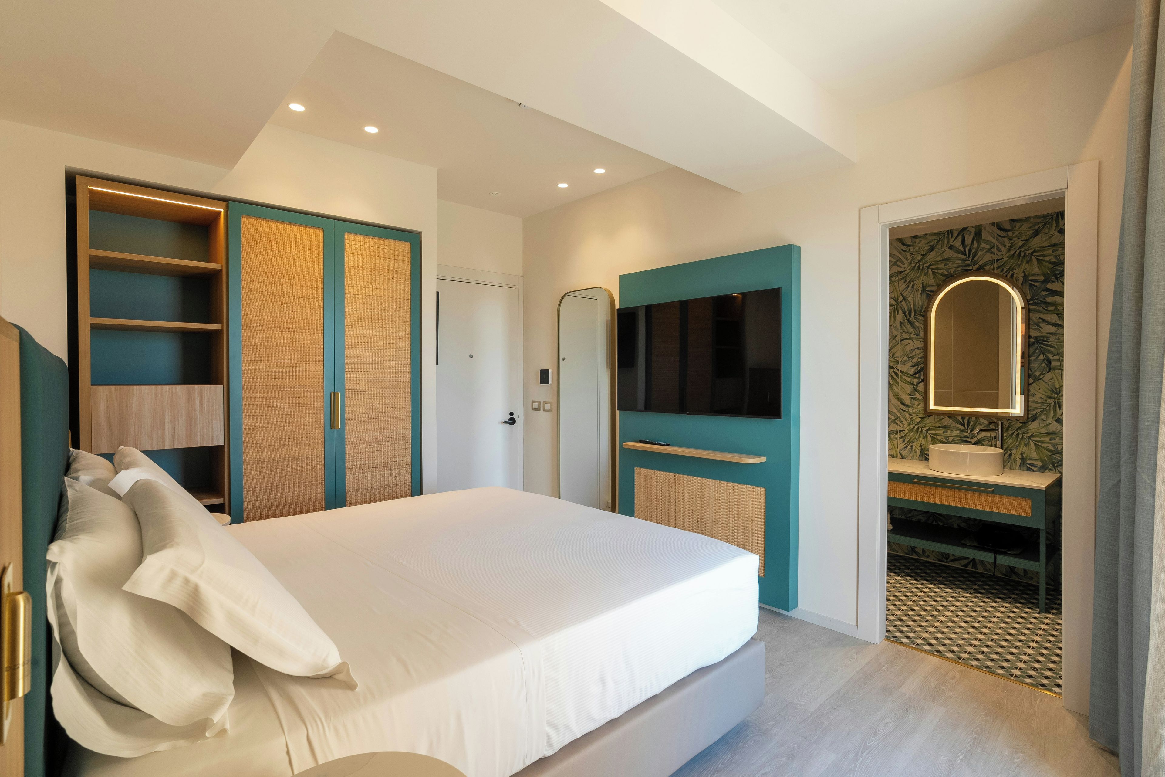 Ein modernes Schlafzimmer mit einem großen Bett, einem Einbauschrank und einem Badezimmer mit Spiegel und Waschbecken.