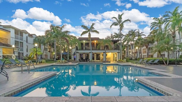 A swimming pool surrounded by palm trees and buildings with balconies. - FTL 1BR Near Beach | Pool + Free Parking (Fort Lauderdale)