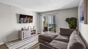 A modern living room with a sofa, a TV mounted on the wall, a wooden console table, and a large plant. - FTL 1BR Near Beach | Pool + Free Parking (Fort Lauderdale)
