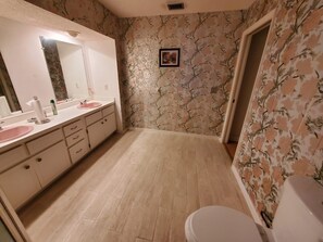 Un baño con piso de madera, un lavamanos blanco con lavabo rosa, un espejo y un inodoro.