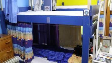 A bunk bed with a blue top bunk, a lower bunk with a curtain, a wooden dresser, and a radiator.