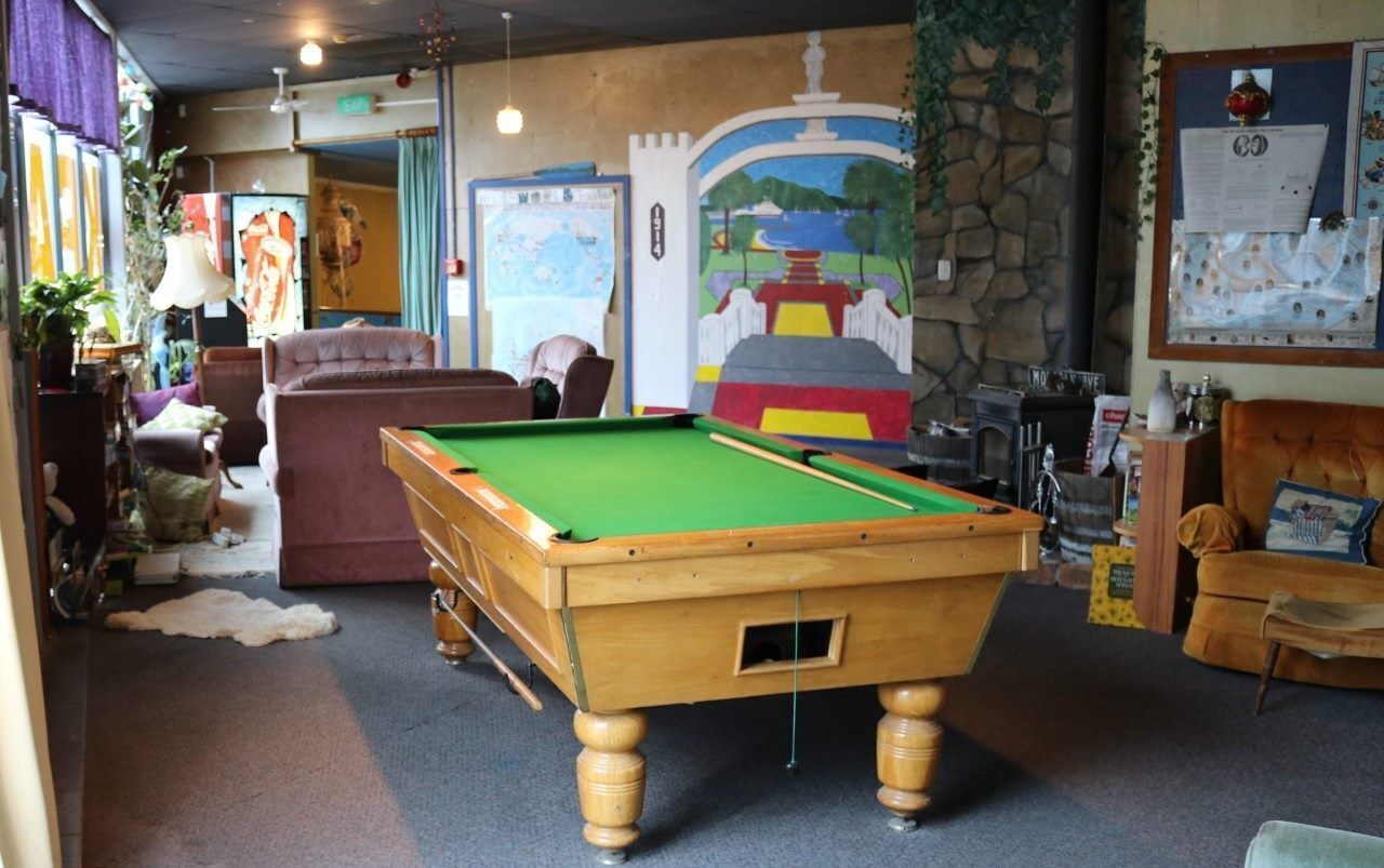 A pool table in a room with a mural, a sofa, and a bulletin board.