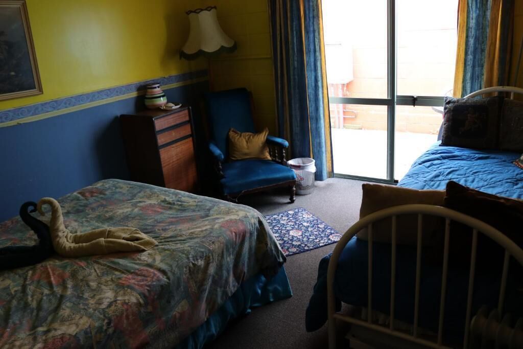 A room with two beds, a chair, a dresser, and a window with curtains.