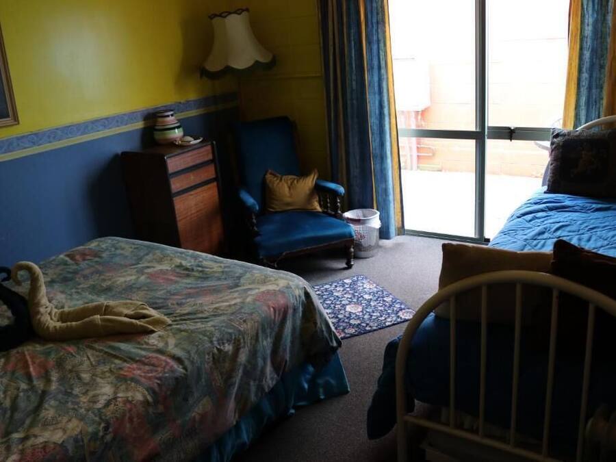 A room with two beds, a chair, a dresser, and a window with curtains.