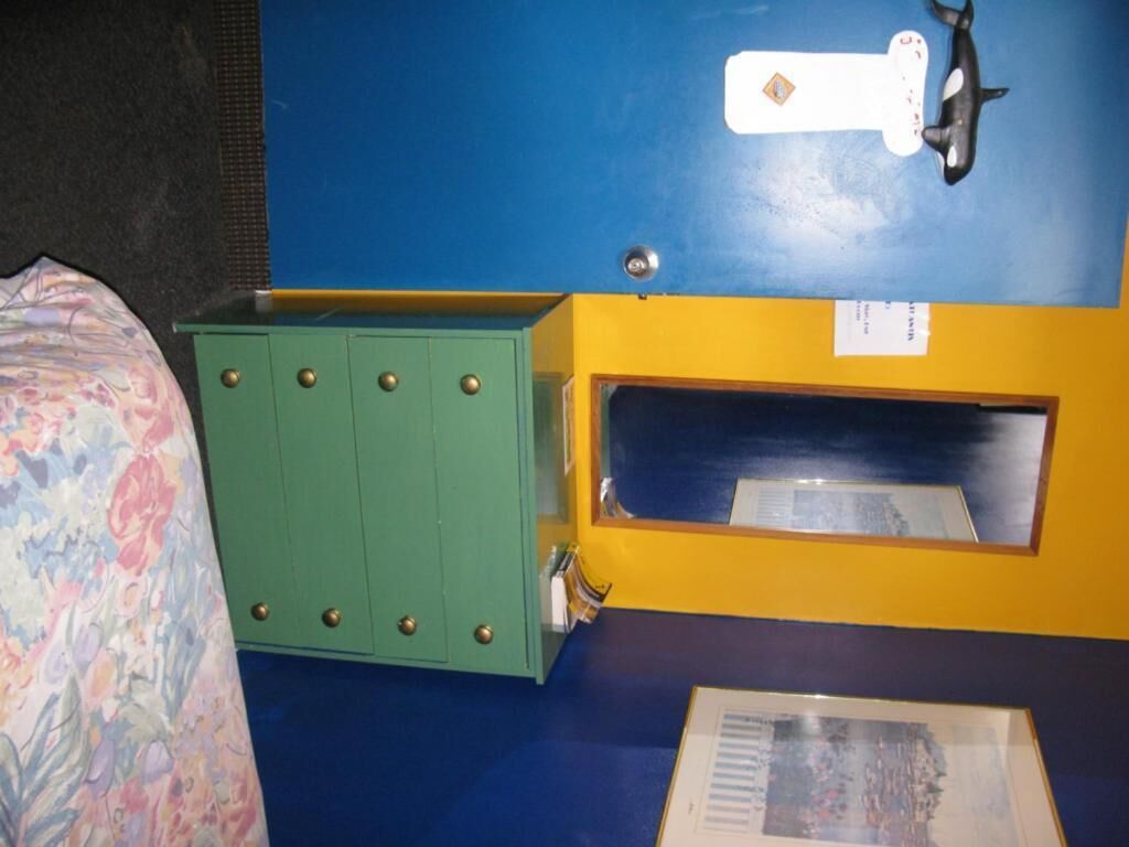 Una stanza con un letto, un armadietto verde, una parete gialla e una finestra.