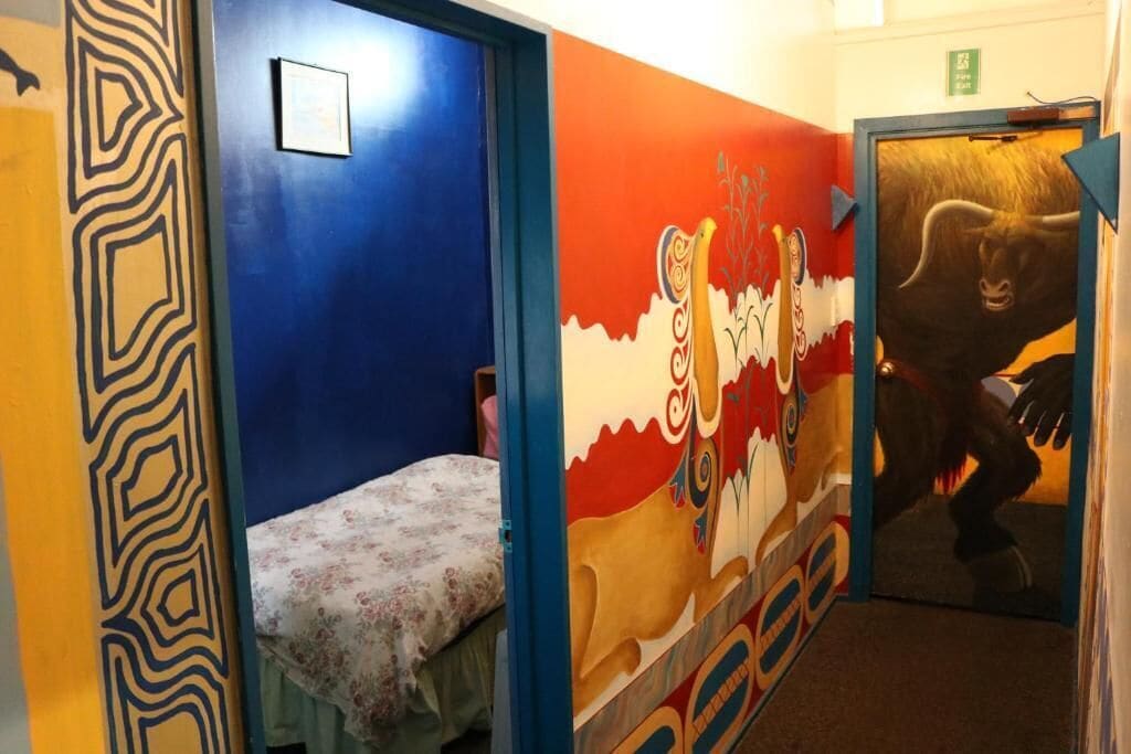 Ein Zimmer mit einem Bett, einer Wand mit einem Wandgemälde und einer Tür mit einer Stierdarstellung.
