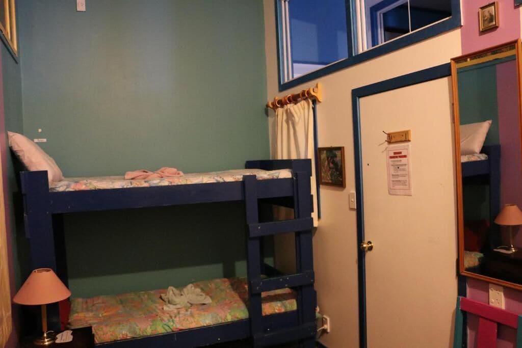 A bunk bed room with a door, a small table with a lamp, and a mirror on the wall.