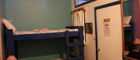 A bunk bed room with a door, a small table with a lamp, and a mirror on the wall.