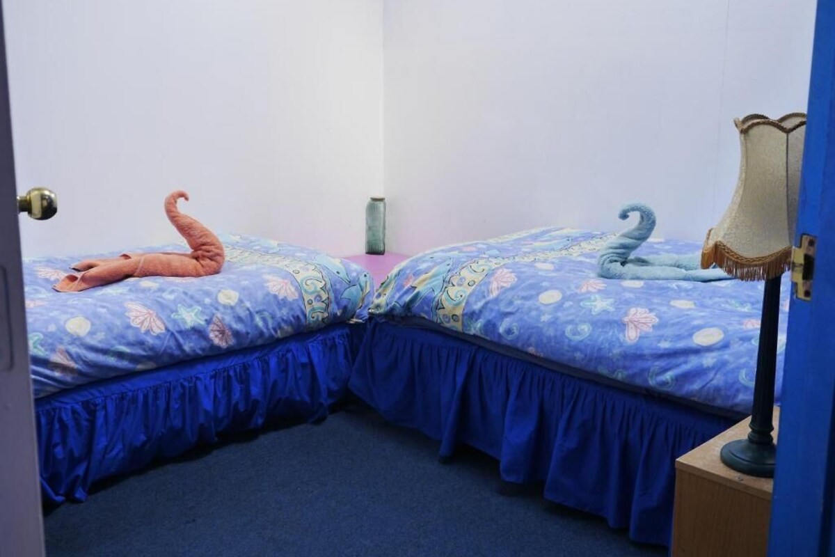 Una habitación con dos camas, cada una con una decoración de color diferente, una mesita de noche y una lámpara.