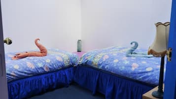 A room with two beds, each with a distinct color theme, a bedside table, and a lamp.