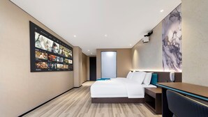 Une chambre d’hôtel moderne, dotée d’un grand lit, d’un bureau et d’un téléviseur fixé au mur, qui diffuse différentes émissions.
