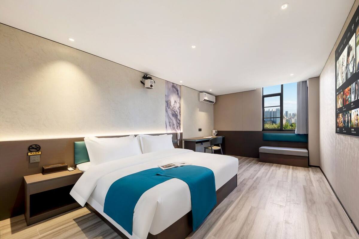Ein modernes Hotelzimmer mit einem großen Bett, Nachttischen, einem Schreibtisch und einem Fenster mit Blick auf die Stadt.