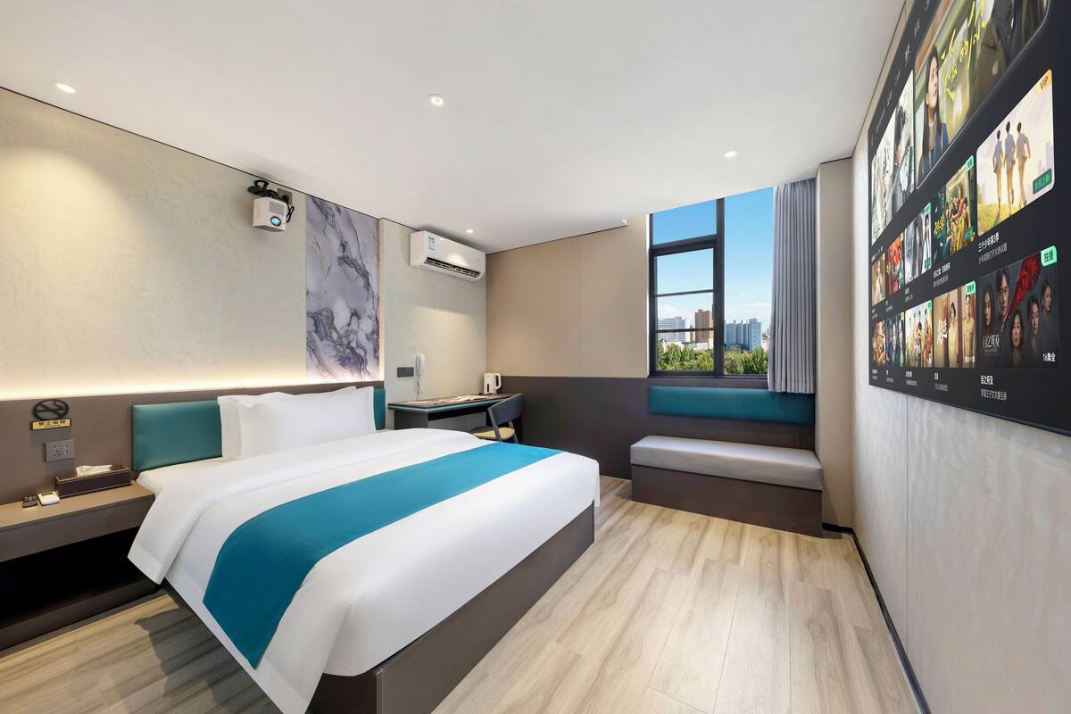 Ein modernes Hotelzimmer mit einem großen Bett, einem Schreibtisch, einer Sitzecke und einem an der Wand befestigten Fernseher, der verschiedene Sender zeigt.