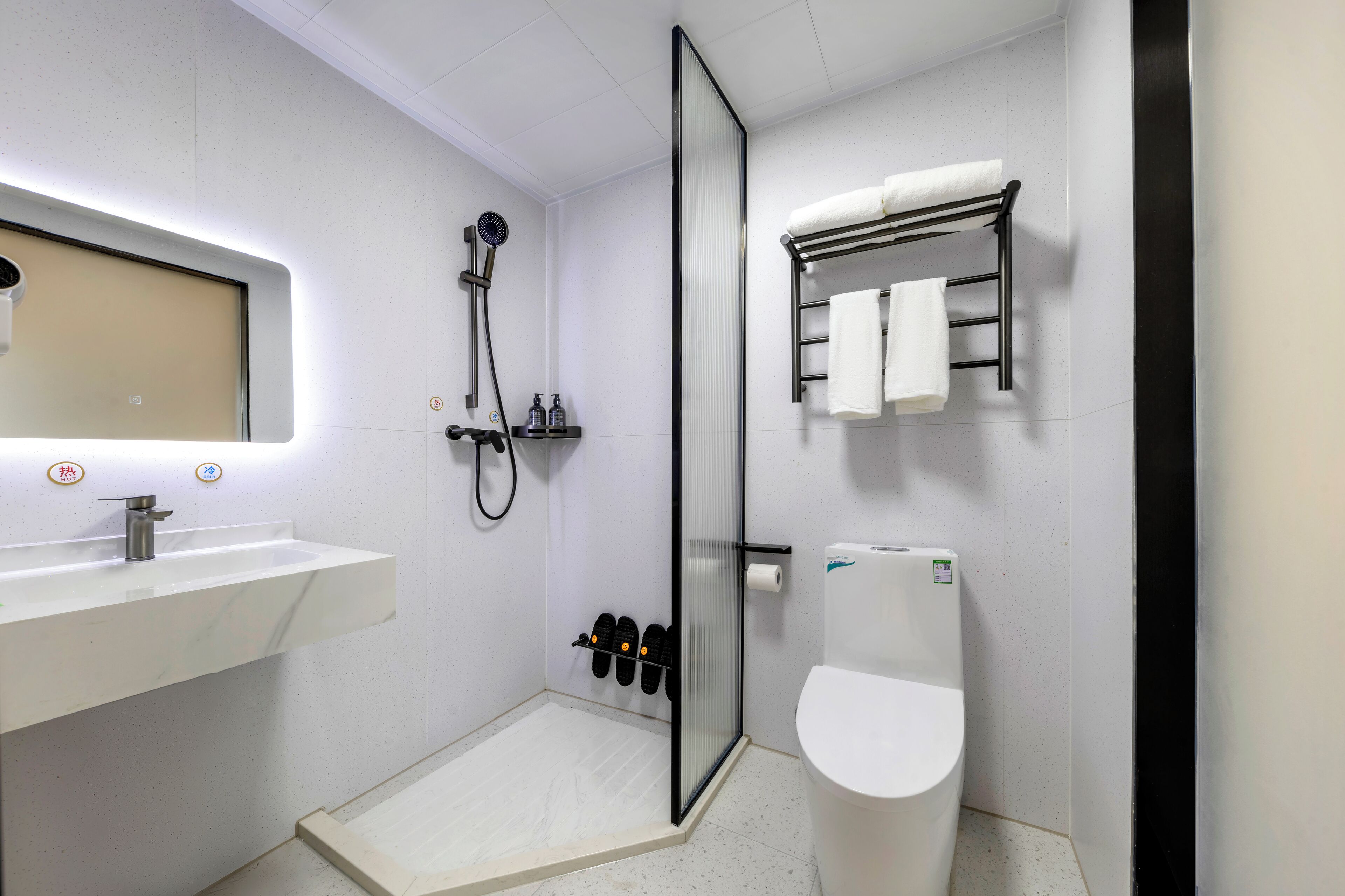 Un baño moderno con lavamanos blanco, cabina de ducha de cristal, inodoro y perchero para toallas.