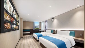 Une chambre d’hôtel avec deux lits, un bureau, une chaise et un grand téléviseur fixé au mur, qui diffuse des affiches de films.