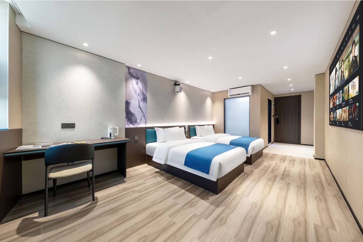 Ein modernes Hotelzimmer mit Schreibtisch, zwei Betten, einem großen Kunstwerk an der Wand und einem digitalen Bildschirm, der Inhalte anzeigt.