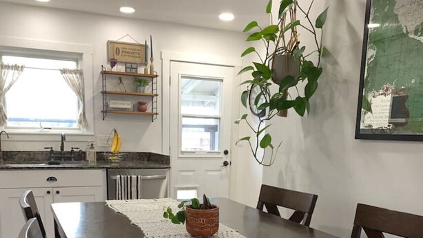 A dining area with a wooden table and chairs, a white macrame runner, and a hanging plant. - Wine Country Cottage Escape (Fulton)