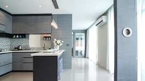 A modern kitchen with a central island, dark cabinetry, and a tiled backsplash. - Stylish 2BR Condo in Citygate Phuket – Walk to Beach, Clean & Breezy Stay (Kamala)