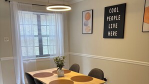 Uma sala de jantar com uma mesa de madeira, cadeiras pretas, um tapete estampado e uma luminária no teto.