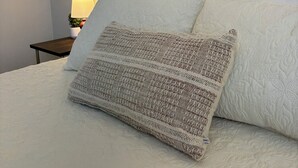 Uma cama bem arrumada com almofada decorativa estampada, cabeceira decorativa e luminária de cabeceira.