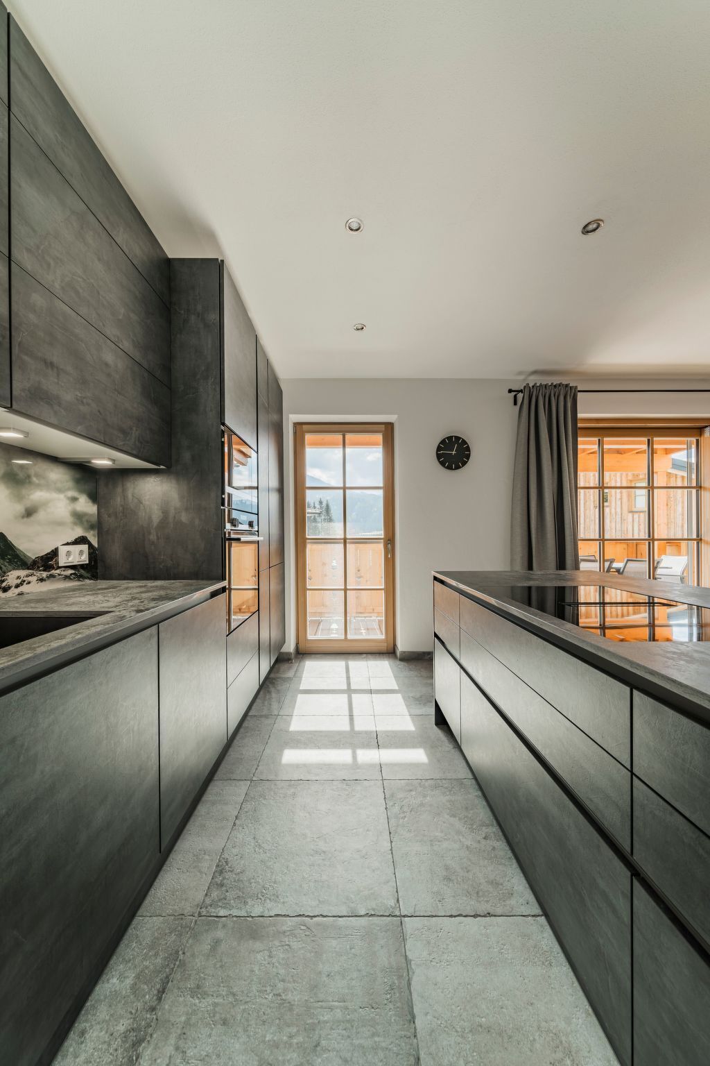 Een moderne keuken met donkere kasten, een centraal eiland en uitzicht door een groot raam.