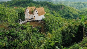 Ein rustikales, weißes Gebäude mit strohgedecktem Dach, umgeben von üppiger Vegetation und einer gebirgigen Landschaft.