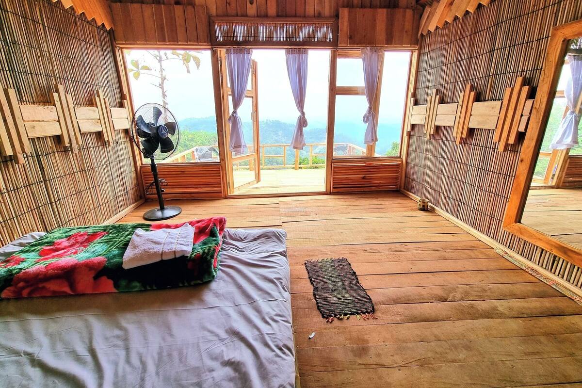 Habitación de cabaña de madera con una cama, un ventilador y vistas al exterior.